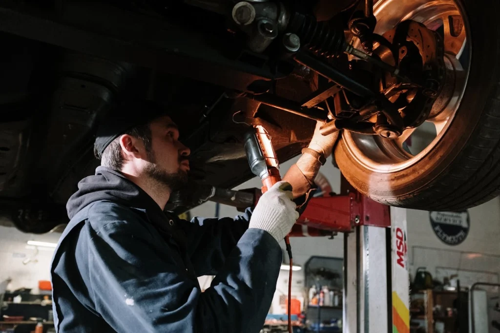 mechanic examining cars undercarriage at a garage, focusing on vehicle maintenance.