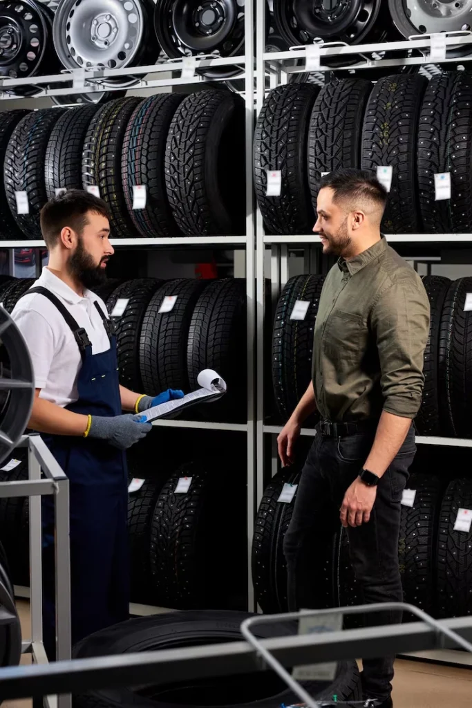 seller auto mechanic helping man choose tires car store showing giving information about best one